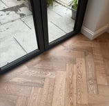 A brown oak herringbone floor with a border against folding doors