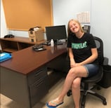 a teacher sitting at a desk with a clock on the wall