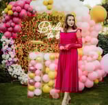a woman in a red dress standing in front of a pink and gold balloon filled