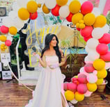 a woman in a white dress standing in front of a large arch shaped balloon