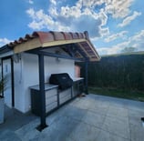 Structure métallique sur mesure pour cuisine extérieure avec auvent en tuiles, conçue par un métallier ferronnier à proximité