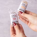 two hands holding two packages of cocoa beans