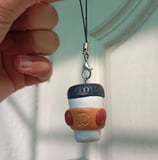 a person holding an engraved white brown coffee cup shaped clay keychain  