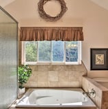 Bathroom with a built-in soaking tub beneath a window and a wreath above.