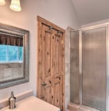 Rustic bathroom view with a wooden door, vanity mirror, and glass shower enclosure.