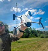 Dronepiloot toont DJI Mini 4 Pro drone in open veld tijdens voorbereidingen voor luchtinspectie op locatie