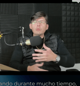 a man in a black jacket and glasses on a microphone
