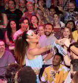 drag performer with dollar bill stuck to forehead in the middle of a crowd accepting tips 