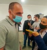 homem à esquerda com camisa cinza e máscara facial azul, mulher à direita com blusa azul e máscara