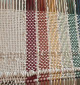 a loom with an unfinished hand-woven towel in muted rainbow pride flag colours