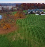 A large house with a spacious yard, a pond, and vibrant autumn-colored trees surrounding the propert