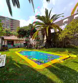 casa con piscina y gran patio verde incluye palmeras y arboles diversos además de un cierre ladrillo