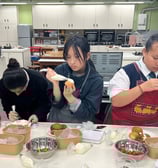 同學們喺設備齊全嘅廚房中專注裝飾甜點,使用唧花袋為 泡芙加上糖霜和士多啤梨裝飾,營造出互動學習嘅熱鬧氛圍