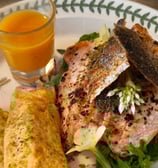 Rolled egg, salmon with crispy skin, wild garlic flower garnish, sea buckthorn juice