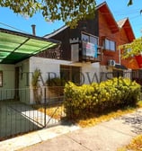 casa dividida color café con reja baja de acero y arbustos , estacionamiento tipo quincho