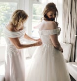 a woman in a white dress is helping a woman in a wedding dress