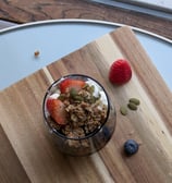 a cup of parfait with yogurt, granola, pumpkin seeds and berries