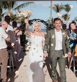 a man and woman walking down a beach wedding ceremony