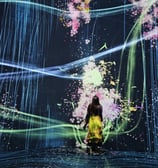 a woman in a yellow dress standing in front of a large screen with a painting