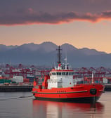 A maritime patrol vessel with the identification 'GC 77' is navigating through waters. The ship's hull is marked with the word 'PREFECTURA' and an anchor symbol. The vessel is set against a backdrop of greenery and urban architecture, with flags visible near the top.