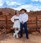 a man and woman in cowboy attire standing in front of a wagon