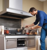 A tidy kitchen corner with a silver refrigerator, white cabinets, and various kitchen appliances on the countertop, including a kettle and a dish rack. There is a blue wall hanging featuring a white bear and stars on one side, and a small festive decoration hanging on the cabinet door.