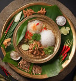 A plate of pad thai garnished with a slice of lime on a leaf, accompanied by chopped green chilies in a small blue bowl. The dish includes noodles, peanuts, and pieces of chicken or tofu, placed on a round woven basket tray.