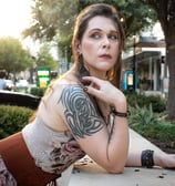 woman leaning on cement wall wearing flower dres with sunset behind her looking wistfully behind her