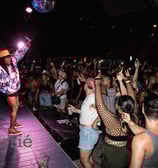 black rapper on stage, arms outstretched while audience close to stage claps with arms raised