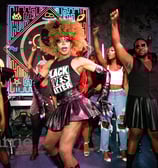 drag queen in "black lives matter" shirt dances toward audience surrounded by dancers.