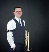George Chase wearing a vest, tie and arm garters, holding a cornet.
