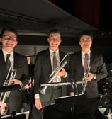 Three men holding trumpets and wearing suits, in an orchestra pit.