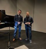George Chase and Caleb Hudson smile, holding piccolo trumpets, during a rehearsal break.