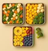 Stainless steel trays with frozen broccoli, cauliflower, carrots, mango cubes, pineapple, banana sli