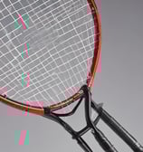 A worn badminton racket with a red and white frame is resting on a moss-covered concrete step. The racket's strings are slightly sagging, indicating it is old or well-used. The surrounding surface has patches of green and gray, with some small stones and worn areas visible.