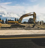 Escavadeira e maquinário pesado em um canteiro de obras, preparando o terreno para construção sob um céu azul com nuvens.