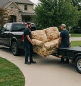 Two men hauling an old couch into the back of a black RAM pickup truck.