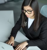 a woman in a suit and glasses is typing on a laptop