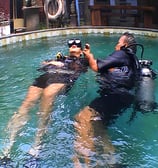 a dive master and student in scuba gear in a pool geting the introduction dive course