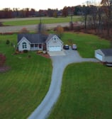 A country house with a separate garage and a long driveway, surrounded by open land.