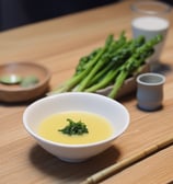 A beautifully arranged scene with a ceramic jar, a bamboo matcha whisk in a holder, a bowl with floral patterns, and a pair of chopsticks resting on a blue fabric napkin. The setting evokes a peaceful, traditional aesthetic, possibly related to Japanese tea culture.