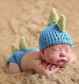 a baby boy wearing a blue crochet dinosaur hat and pants