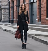 A person in a stylish black outfit, featuring a blazer and a uniquely designed top paired with high-waisted pants. The clothing appears sophisticated and tailored, emphasizing modern fashion trends.
