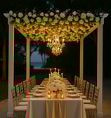 Elegant outdoor dining event under a pergola with luxury table settings, floral arrangements, and ambient lighting by Las Car