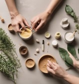A hand is holding a bar of handmade soap with a label that reads 'Vya Naturals' featuring ingredients like activated charcoal and cedarwood. The background includes pieces of black soap or material placed on a wooden surface.