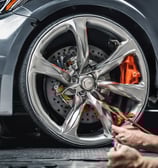 A car service workshop with prominent signage advertising its specialization in automotive air conditioning. Several cars are parked in front, including a red SUV and a white sedan. The building has large signs in Indonesian and a blue banner with the text 'BENGKEL RESMI' and 'AGAM AC'.