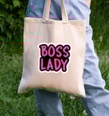 a person holding a tote bag and a written text on bag is "Boss lady".