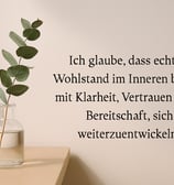 Minimalistische Szene mit Eukalyptuszweig in Glasvase am Fensterbrett und Zitat über inneren Wohlsta