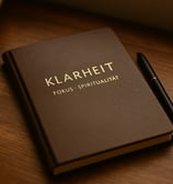 Dunkelbraunes Notizbuch mit der Aufschrift „Klarheit – Fokus – Spiritualität“ und Stift auf Holztisc