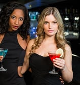 Two stylish women holding colorful cocktails at a sleek Las Vegas bar, showcasing the upscale downtown nightlife vibe.